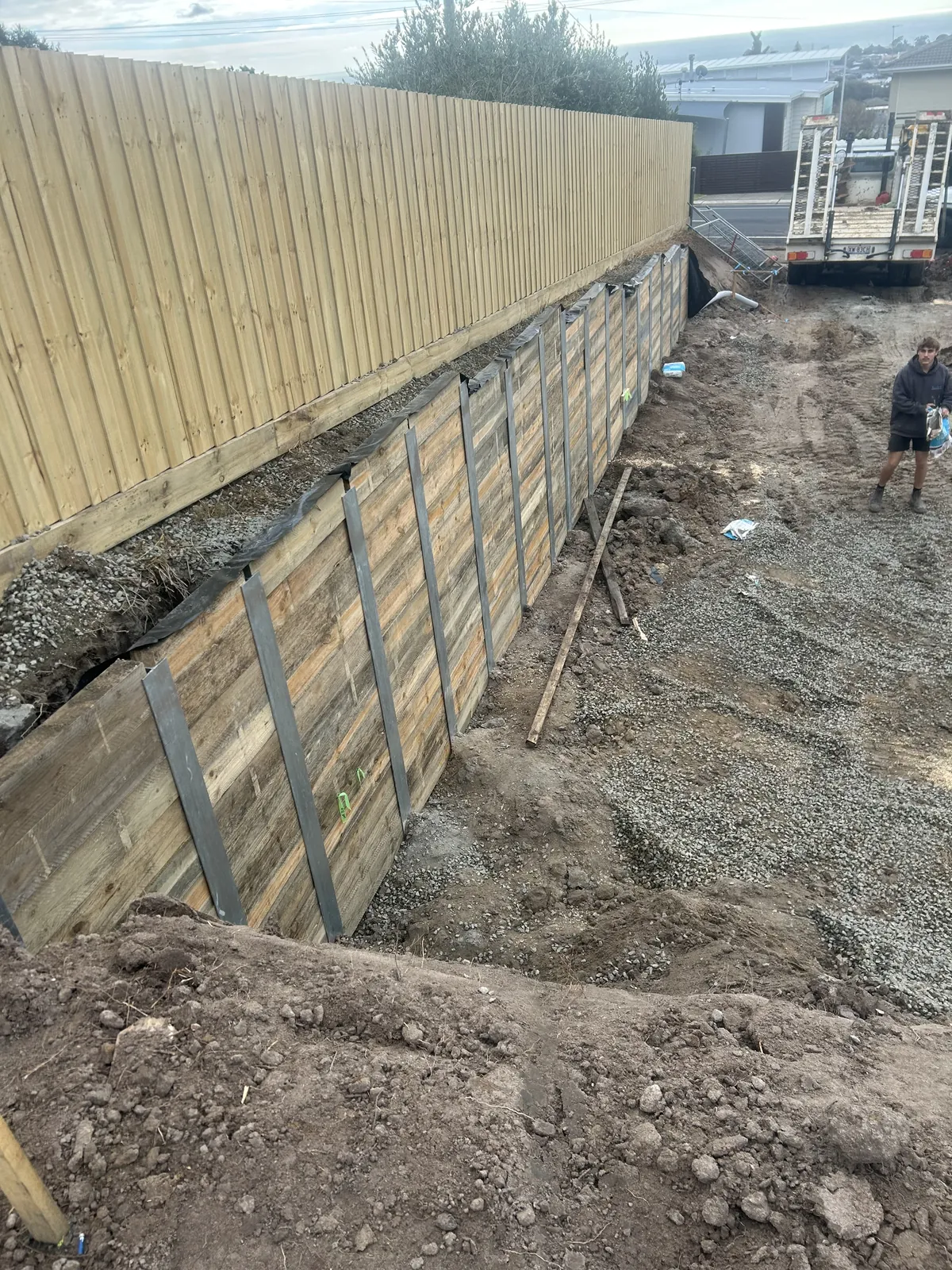 Timber sleeper wall going in behind a new paling fence, with drainage membrane and gravel backfill