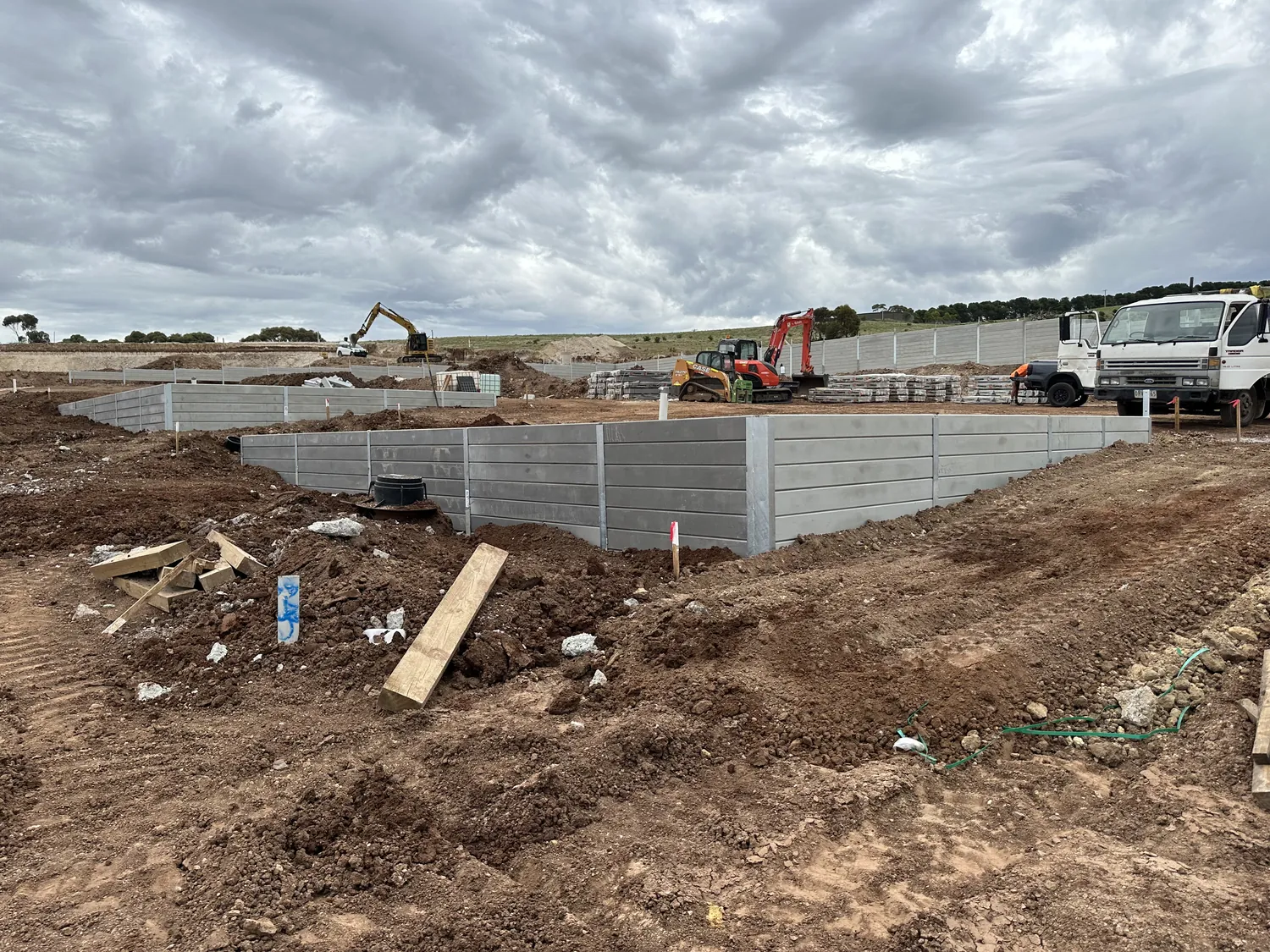 Large commercial grey sleeper retaining wall with machines and material stacks on site