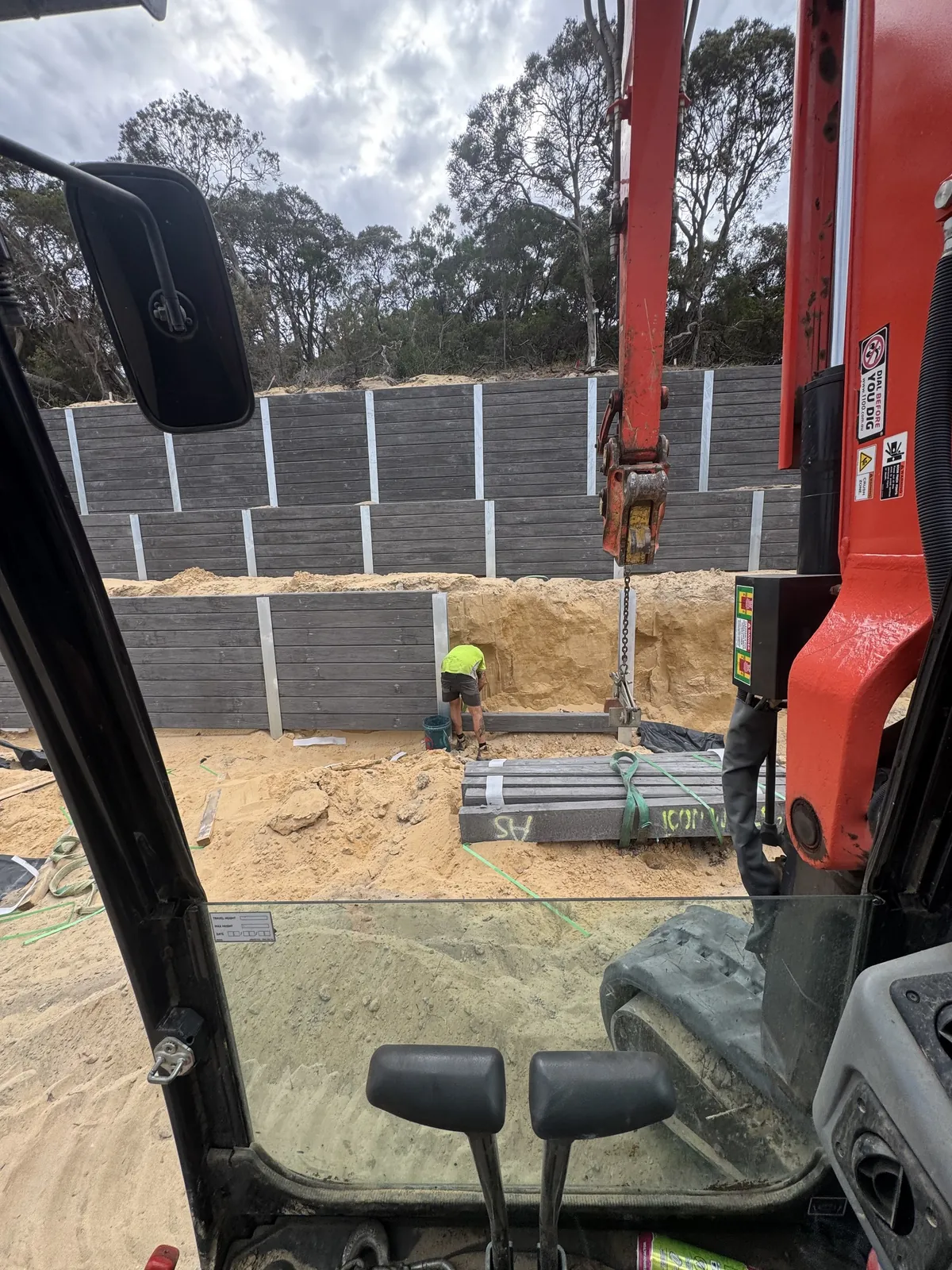 View from the excavator cab as a tiered charcoal sleeper wall is craned into place