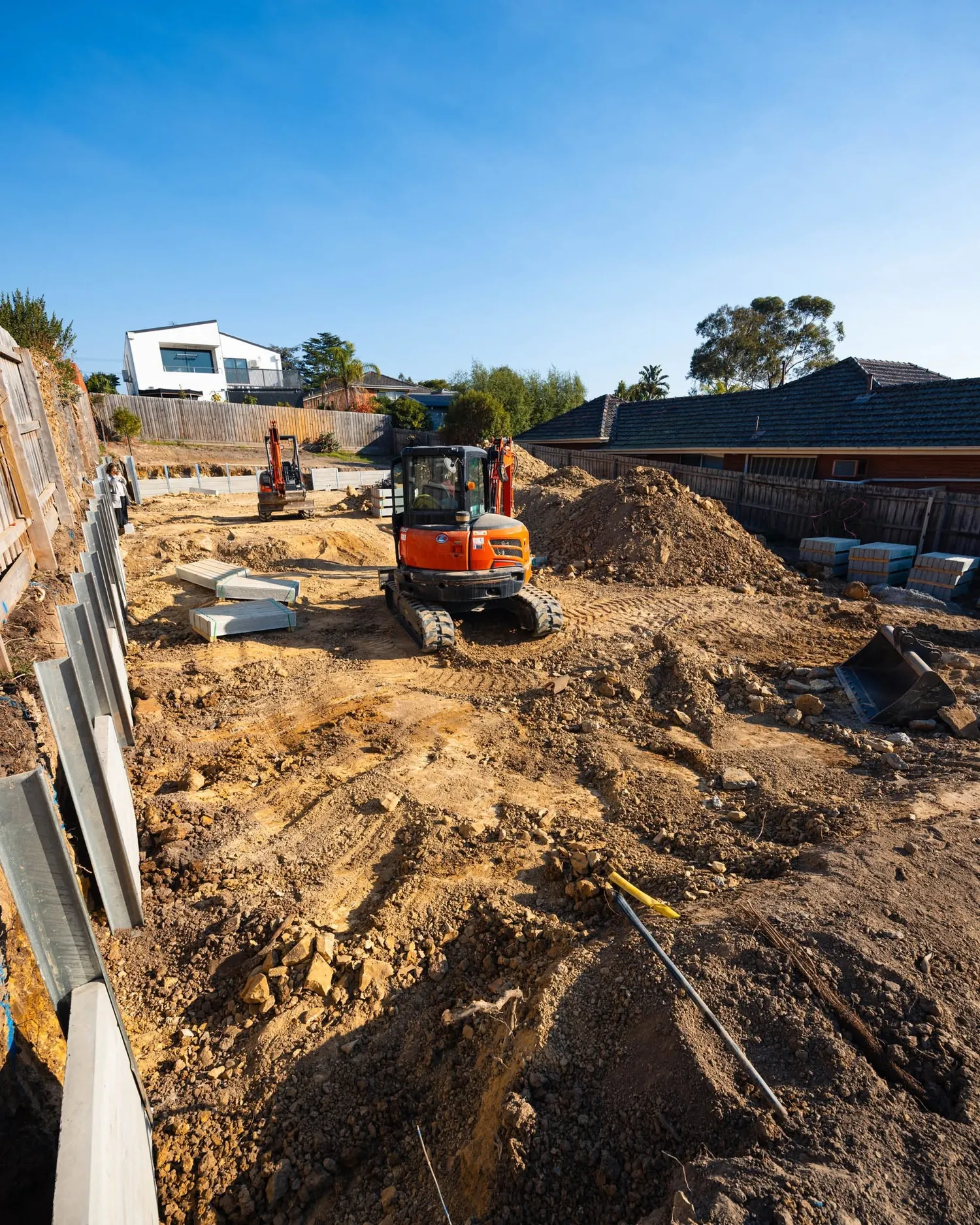 Two Align excavators cutting a residential block with sleepers and posts stacked ready to go in