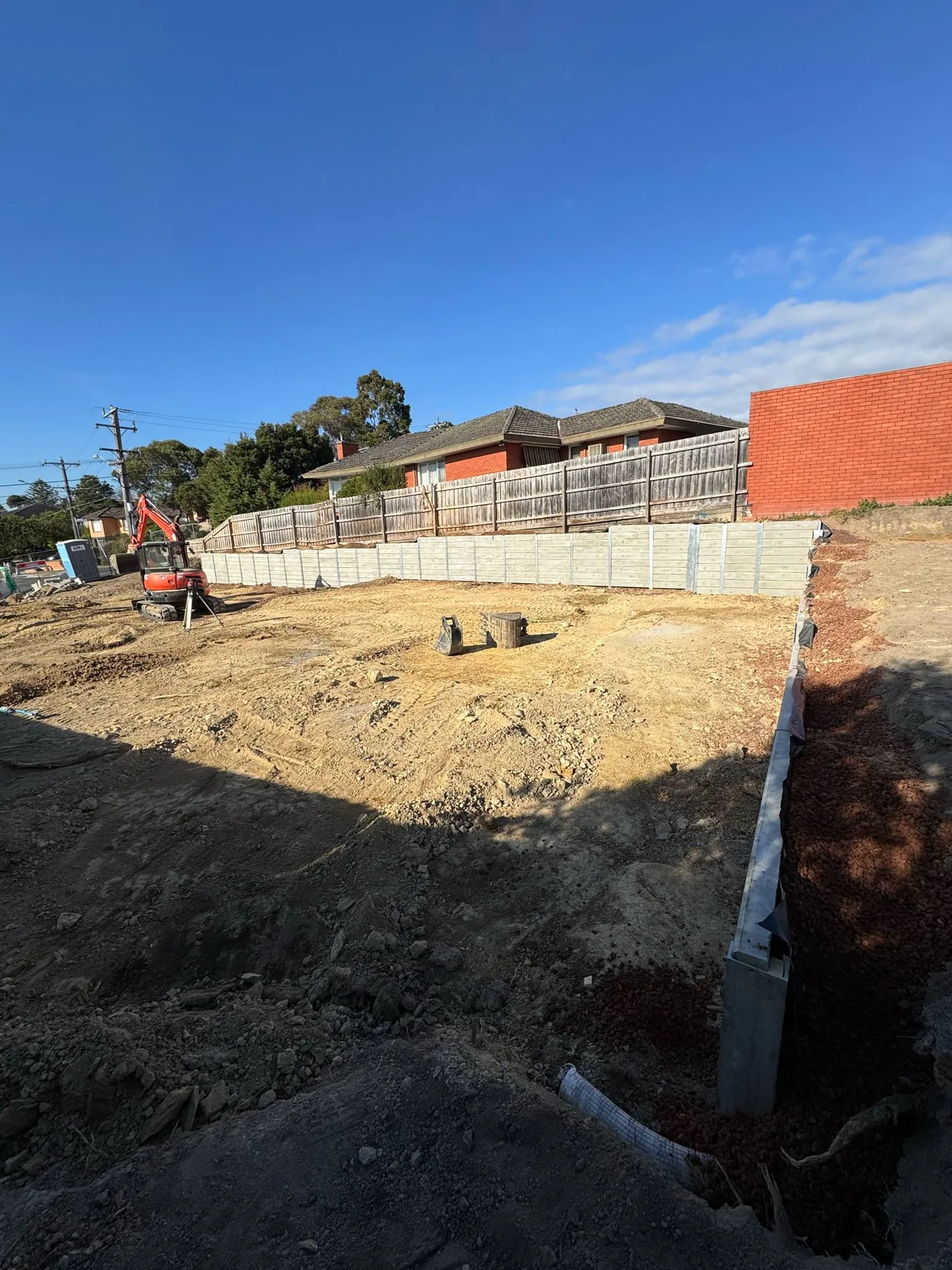 Align excavator beside a finished grey sleeper retaining wall on a residential block